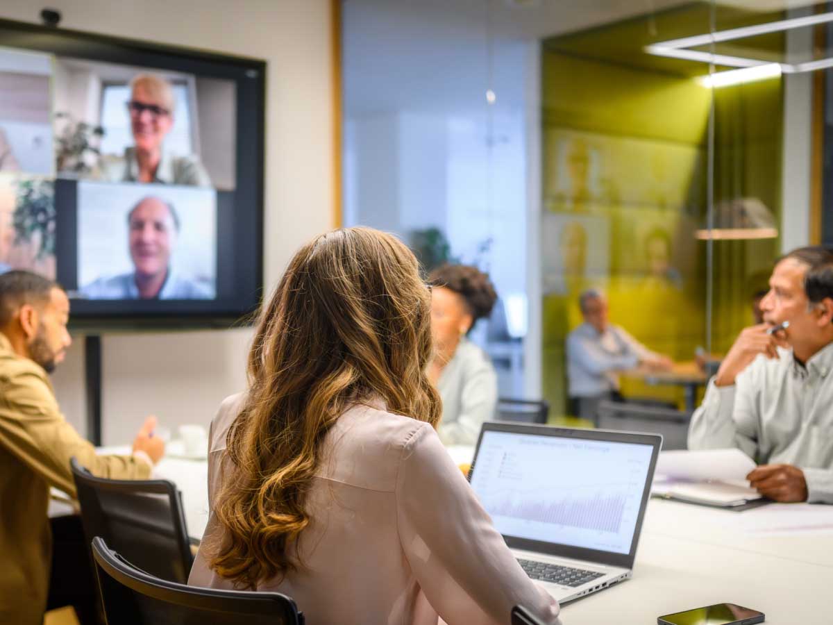In-office employees sitting at a conference room table while looking at remote employees on screen.