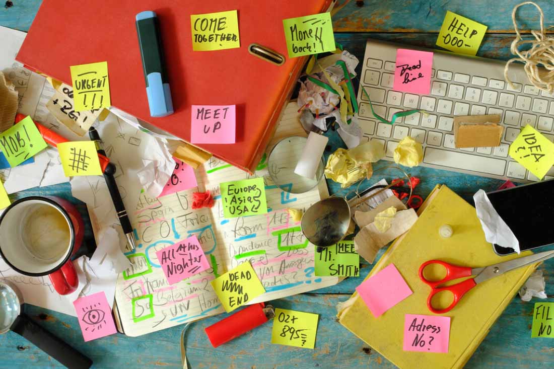 Cluttered desk with sticky notes, papers, and office supplies.