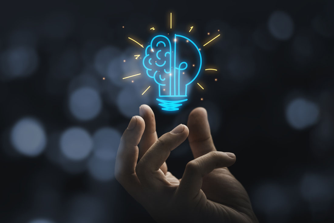 A hand holding a glowing brain-shaped light bulb.