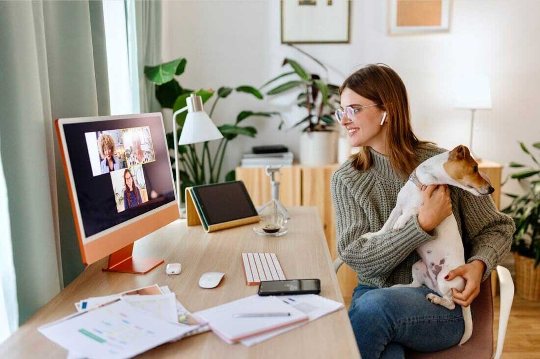 A woman working from home for a hybrid company on a zoom call with her dog.