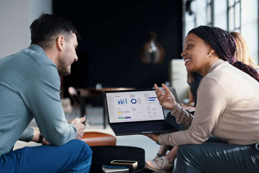 Two colleagues discussing business analytics while reviewing data visualizations on a laptop screen.