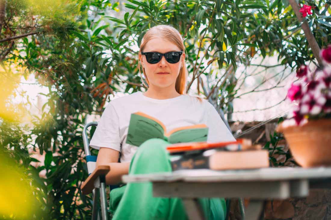 Woman reading a book outdoors while wearing sunglasses.